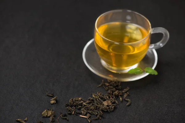 Té negro en una taza de vidrio y hojas de té sobre fondo de piedra negra — Foto de Stock