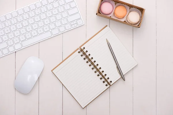 Escritorio blanco con macarrones coloridos, teclado y cuaderno abierto . — Foto de Stock