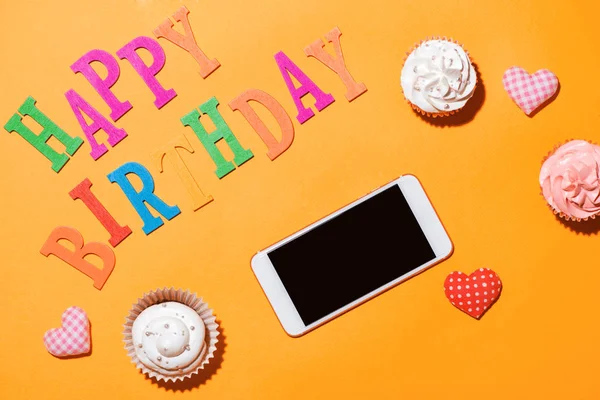 Woorden Happy Birthday met cupcake en smartphone op gele backg — Stockfoto