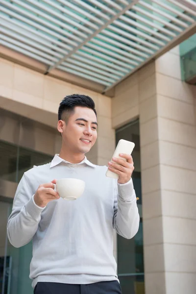 Bonito jovem bebendo café e usando telefone celular no cit — Fotografia de Stock