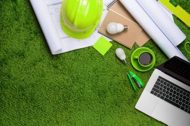 Çalışma alanı ile kask, planları, dizüstü bilgisayar ve çim b üstünde not etmek