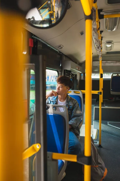 Asiático hombre sentado en la ciudad autobús, escuchar música y buscando th — Foto de Stock