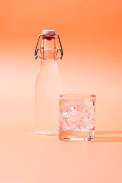 Beber água em uma garrafa e um copo de gelo sobre laranja backgrou — Fotografia de Stock