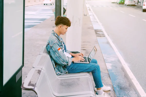 Asian young man sitting on the chair at the airport bus stop and — Stock Photo, Image