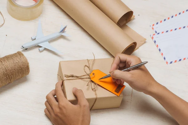 Male hand writing on luggage tag on brown paper parcel — Stock Photo, Image