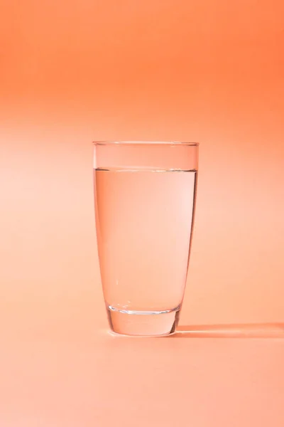 Agua potable en un vaso sobre fondo naranja . — Foto de Stock