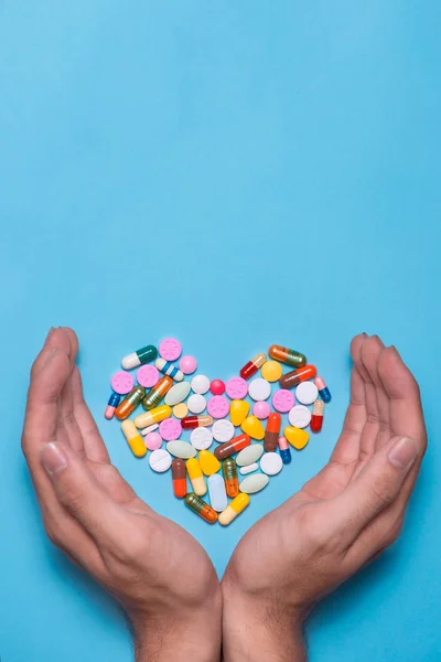 Píldoras de color en forma de corazón cubierto con las manos en el fondo azul — Foto de Stock