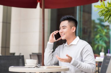 Kafede kahve içme ve akıllı telefonunu kullanarak çekici bir genç adam.