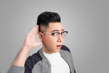 İşadamı yakından gri arka plan üzerinde dinleme kulağının arkasında el ile