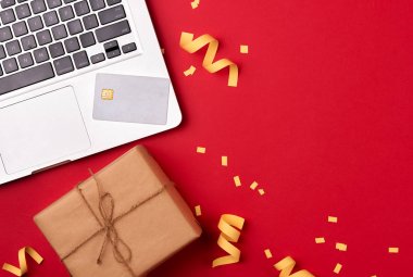 Online Kredi kartı ile Noel tatili için alışveriş. Kırmızı zemin üzerine masada hediyeler ile dizüstü bilgisayar