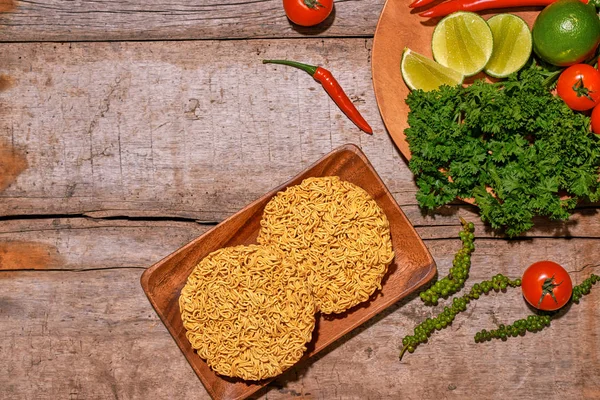 Raw asian instant noodles on wooden board with vegetables