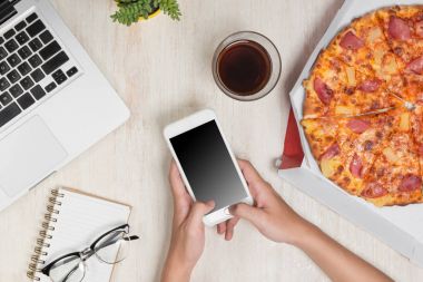 Smartphone ve lezzetli pizza malzemelerle ahşap masa üzerinde tutan adam.