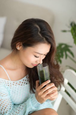 Gülümseyen genç Asyalı kadın evde cam yeşil taze sebze suyu ya da iki yüzlü içme