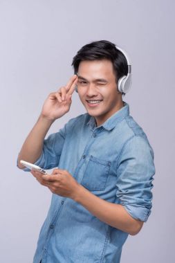 Kulaklıklar giyen ve cep telefonu gri karşı dururken tutan yakışıklı delikanlı