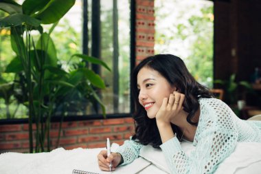 Not Defteri ile yatakta yatarken genç esmer kadın