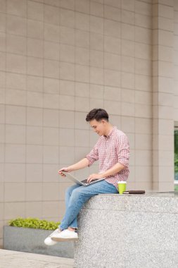 Dizüstü bilgisayar ofis binası dışında oturan genç adam