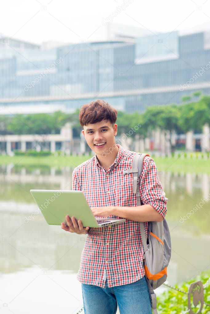 Attractive male asian student using laptop in campus