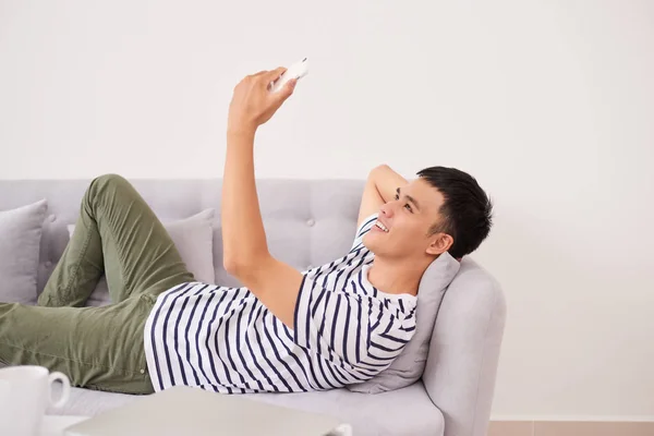 Entspannter Asiatischer Mann Mit Smartphone Auf Couch Heimischen Wohnzimmer Liegend — Stockfoto