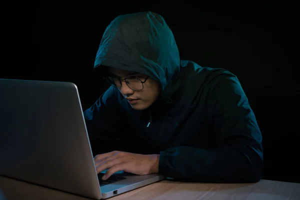 Hacker in a dark hoody sitting in front of a notebook. Computer privacy attack