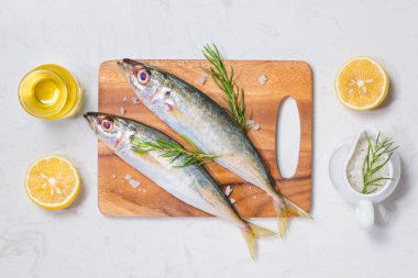 Çeşitli malzemelerle pişirme balık yemek. Limon dilimleri ve ahşap masa üzerinde otlar ile dekore edilmiş taze çiğ balık.