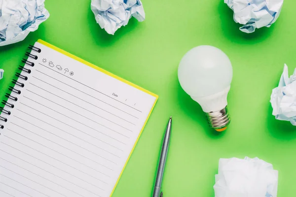 Note book and light bulb on green background.