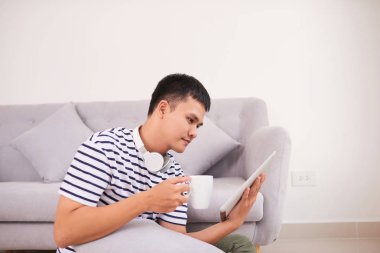 Yakışıklı olan dijital tablet kullanma, kameraya bakıyor ve yerde evde otururken gülümseyen