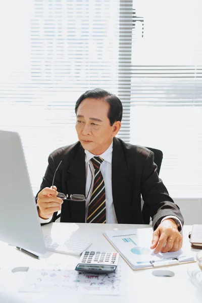 上級金融のアジア系のビジネスマンの彼のワークステーション コンピューターの前に座って — ストック写真