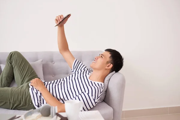 Schöner Asiatischer Mann Entspannt Sich Mit Telefon Auf Der Couch — Stockfoto