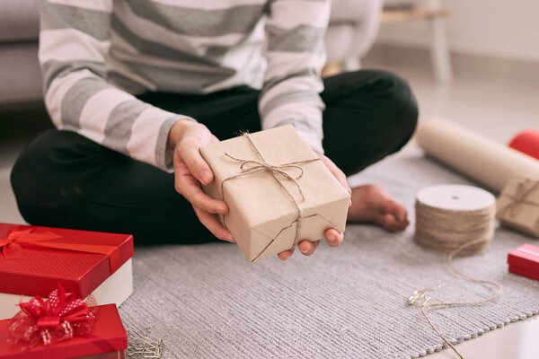 Young happy man packing Valentine gift while sitting on floor