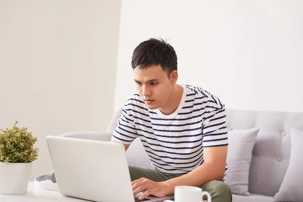 Jovem asiático homem em casa no sofá usando um laptop . — Fotografia de Stock