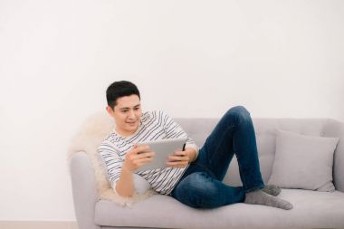 Asya genç adam dijital tablet ile kanepede rahatlatıcı.