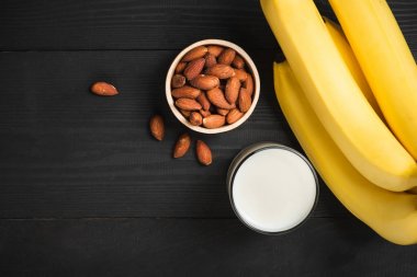 Badem, süt cam ve muz ile siyah ahşap tabloda alan kopyalayın. Sağlıklı yiyecek ve içecek konsepti.