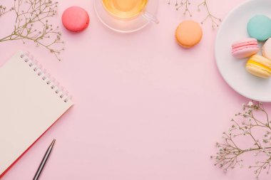 fincan çay, renk macarons, kalem ve pembe masaya çiçek ile boş not defteri