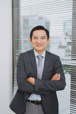 Asya businesman ayakta pencerede gülümseyen.