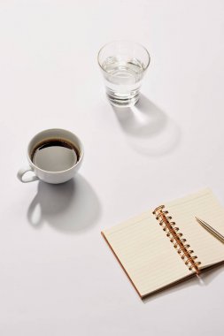 Minimal tarz düz tablo açık defter, kalem cam su ve kahve Kupası ile yatıyordu..