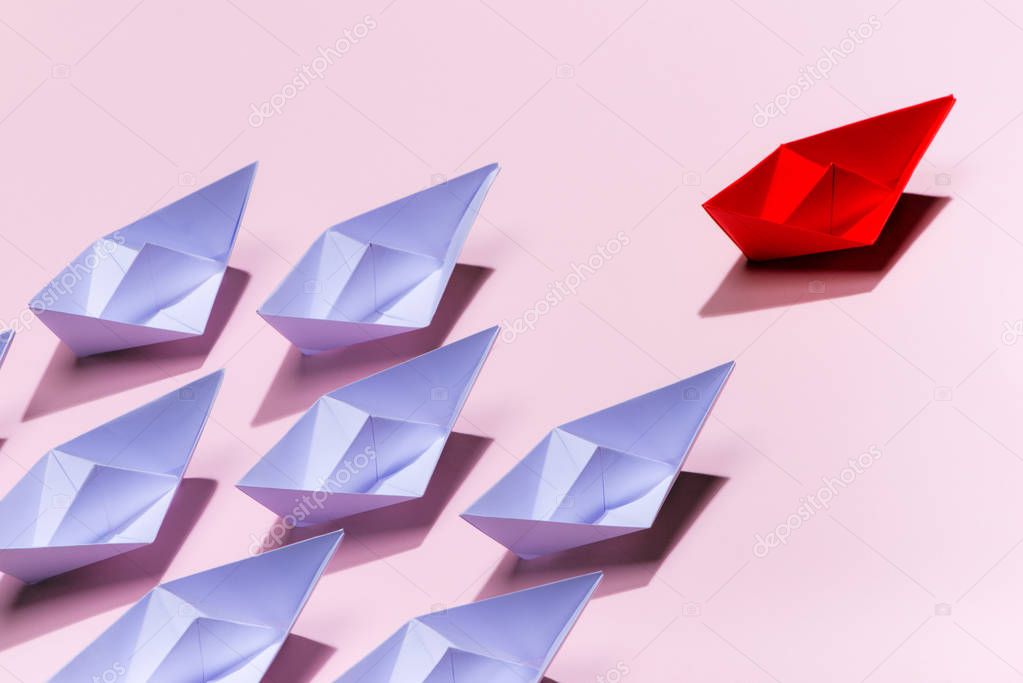Leadership concept. Red paper ship leading among white on pink background.