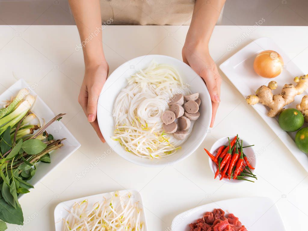 Female chef cooking traditional Vietnamese soup Pho bo with herbs, meat, rice noodles