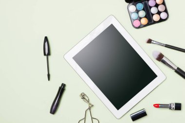 Açık renk arka plan üzerinde dijital tablet ile kozmetik ürünler makyaj düz lay