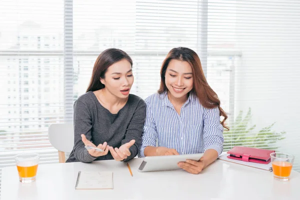 Two smiling asian businesswomen working with laptop in office