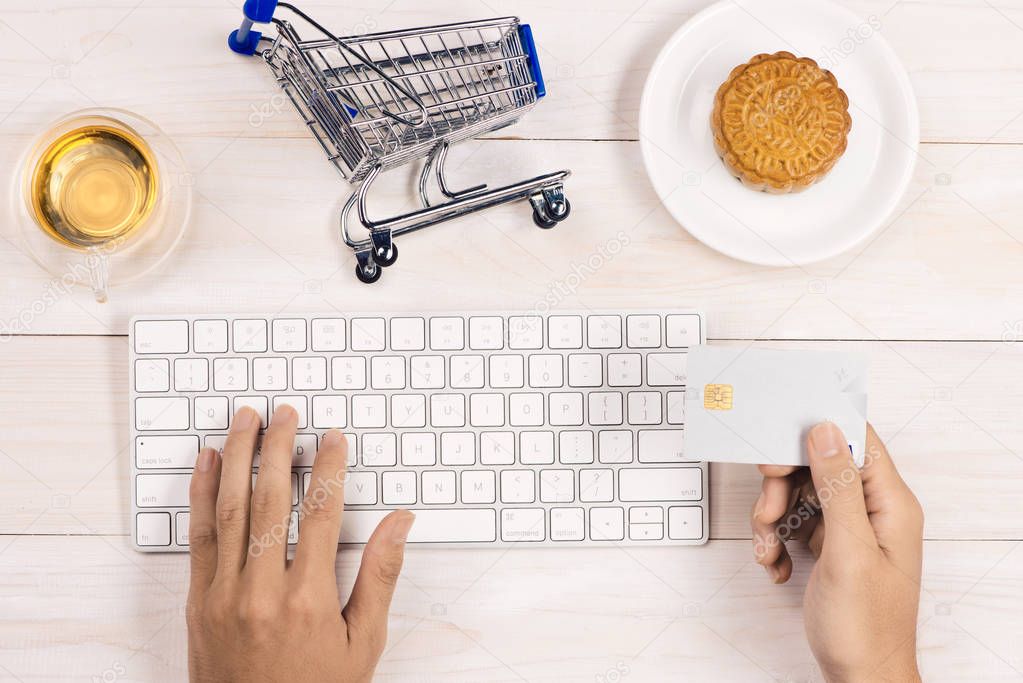 Online shopping concept. Computer keyboard, shopping cart, cake and tea with copy space.