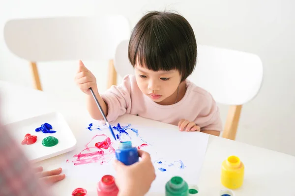 Little asian girl painting with paintbrush and colorful paints