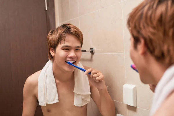 Brushing teeth in morning. Attractive young man brushing teeth with toothbrush, looking at himself in mirror