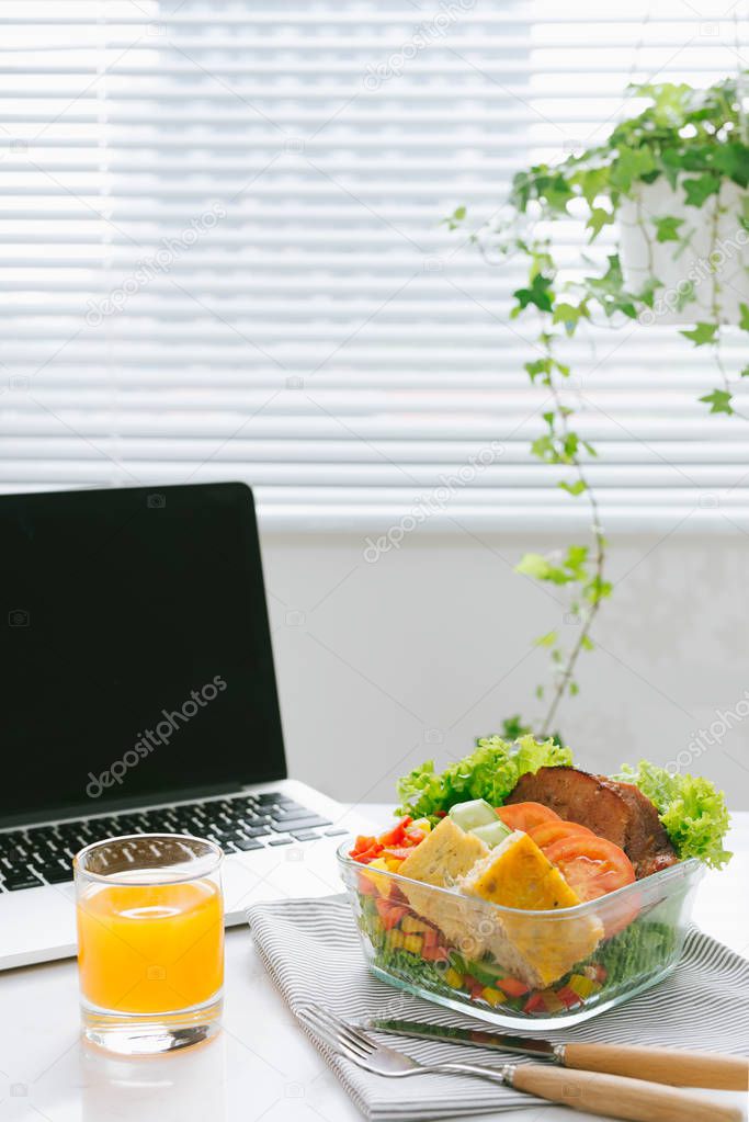 Healthy salad in bowl, orange juice and laptop on office table