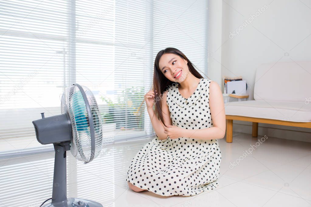 Beautiful aisan woman sitting on living room floor enjoying electric fan cool wind.