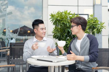 Gülümseyerek, kahve dükkanında konuşurken rahat kıyafetler içinde iki genç yakışıklı iş adamları.