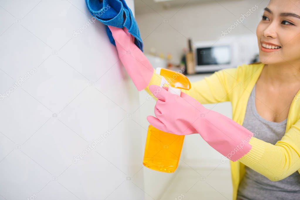 Young asian woman cleaning the kitchen holding detergent spray and cloth