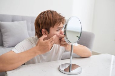 Asian man looking at mirror and popping a pimple clipart