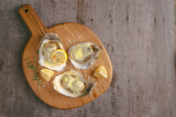 Opened oysters and lemon on wooden board, top view