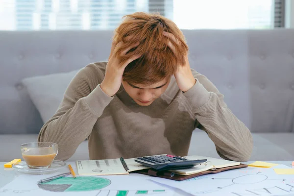 Stressed Asian Businessman sitting at desk with calculator and documents