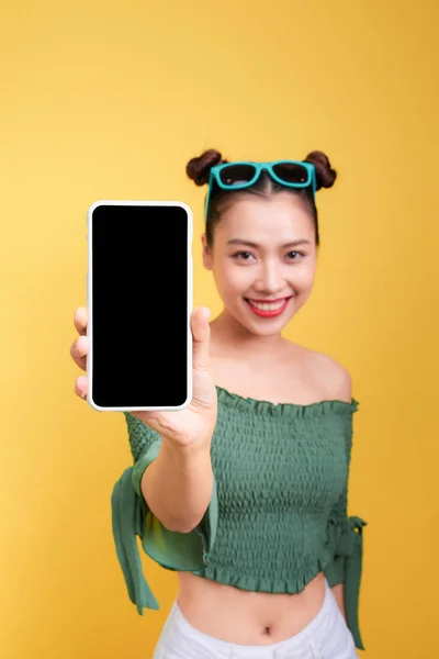 一个开朗可爱的女人的肖像显示空白智能手机屏幕上的黄色背景隔离 — 图库照片